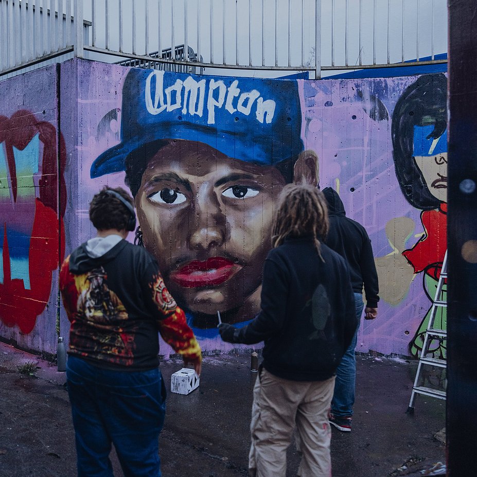 Drei Jugendliche vor einem frisch gesprayte Graffiti