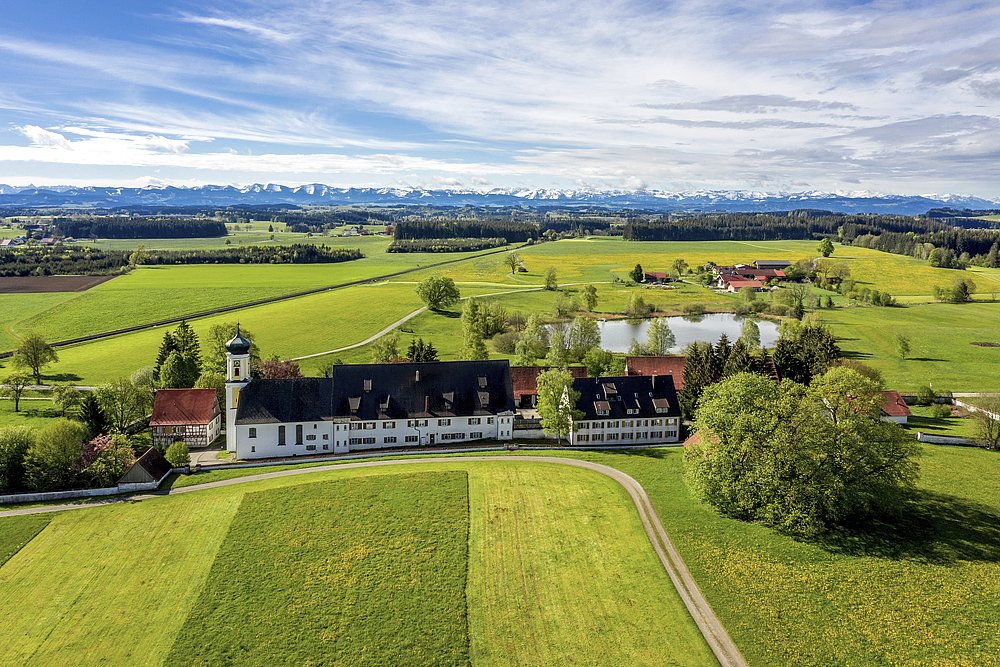 Luftaufnahme der Heimat Bärenweiler im Voralpenland mit See, im Hintergrund die Alpenkette