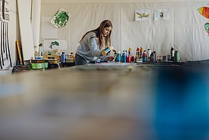 Jugendliche mischt Farben zum Malen an einem großen Tisch Jugendliche mischt Farben zum Malen an einem großen Tisch