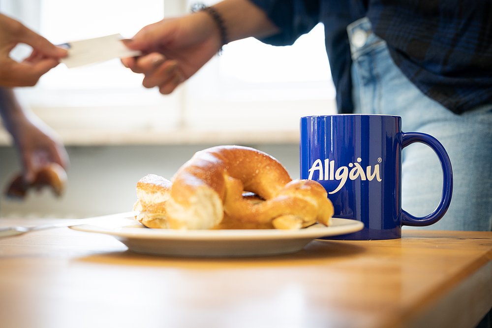 Eine Brezel auf einem Teller und eine Tasse mit einem Allgäu-Logo