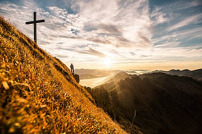 Gipfelkreuz des Siplinger Kopfs, daneben Mann, der in die Ferne über die Berge guckt