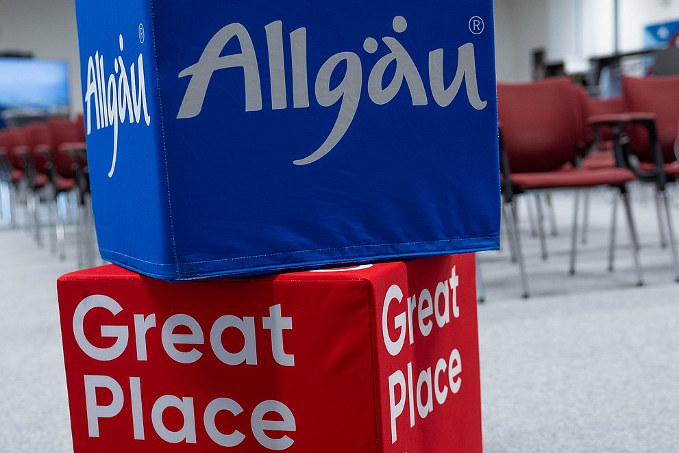 Zwei Würfel aufeinander, unten mit dem Logo von "Great Place to Work", oben das Logo der Allgäu GmbH