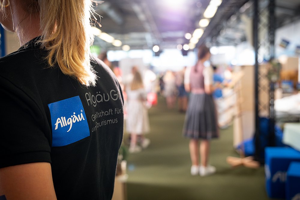 Rücken einer Frau mit T-Shirt mit Allgäu-Logo, im Hintergrund die Festwoche